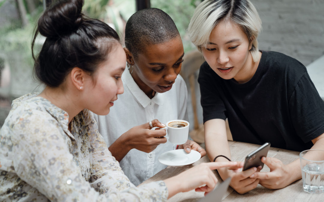 Diverse female friends checking social media on mobile in cafe